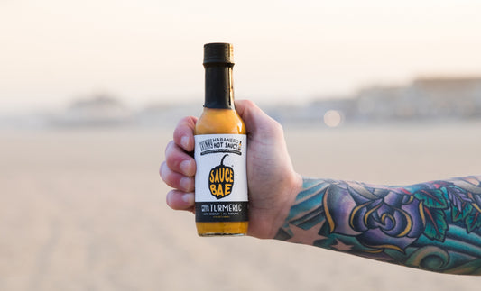 Picture of a tattooed arm holding a bottle of Sauce Bae Skinny Habanero Hot Sauce